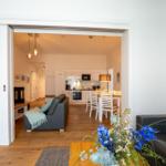 Wohnzimmer mit Sitzgelegenheit, Blick in Küche und Essbereich mit Tisch und Stühlen.
