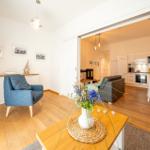 Wohnzimmer mit blauem Sessel und Küche im Hintergrund. Holzboden und modernes Mobiliar.