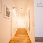 Flur mit Holzboden, weißen Türen und Bildern an der Wand. An der rechten Wand hängt ein Hakenbrett.