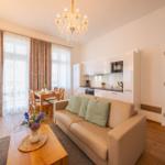 Wohnbereich mit Sofa, Esstisch, Küche und Kaminofen. Holzboden und große Fenster.