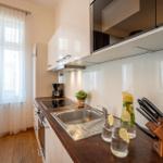 Küche mit Arbeitsplatte, Spüle und Fenster mit weißen Vorhängen.
