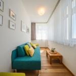 Ein Wohnzimmer mit blauem Sofa, Holzboden und Fenstern mit weißen und braunen Vorhängen.