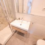 Badezimmer mit Dusche, Waschbecken und Toilette. Wand mit Mosaik und Wellenfliesen.
