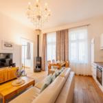 Wohnküche mit Sofa, TV, Esstisch und Kaminofen. Holzboden und weiße Küchenzeile.