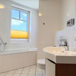 Badezimmer mit Badewanne, Dusche, Waschbecken und Toilette. Fenster mit Jalousie.