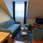 Wohnzimmer mit Sofa, Sessel, Fernseher und Fenster mit Vorhängen.