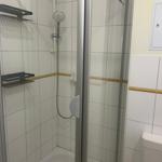 Dusche mit Glaswand, Duschbrause und zwei schwarzen Halterungen an weißen Fliesen.