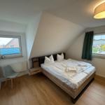 Schlafzimmer mit Doppelbett, zwei Fenstern und Holzboden.