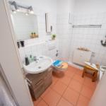 Badezimmer mit Waschbecken, Toilette und Dusche. Weiße Fliesen, orangefarbener Boden und Anker-Dekoration.