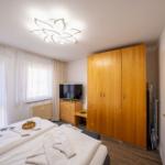 Schlafzimmer mit Bett, Kleiderschrank und TV. Fenster mit Vorhängen und Deckenleuchte.