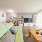 Wohn- und Essbereich mit Sofa, TV und Tisch. Blick auf Terrasse.