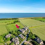 Haus mit Dach und Garten, umgeben von Feldern und Meer.