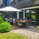 Terrasse mit Tisch, Stühlen und Sonnenschirm neben einem Haus mit Strohdach.