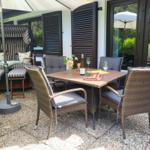 Terrasse mit Sitzgruppe, Tisch und Sonnenschirm. Hintergrund: Haus mit Fenstern und Pflanzen.