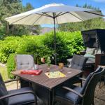 Terrasse mit Tisch, Stühlen, Sonnenschirm und Liegestuhl. Auf dem Tisch liegt ein Spiel.