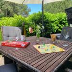 Außentisch mit Brettspiel, Wein und Stühlen unter Sonnenschutz.
