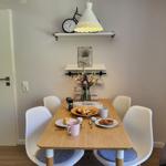 Esstisch mit vier Stühlen, Blumen und Kaffeetassen. Wandregale mit Uhr und Lampe.