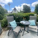 Terrasse mit zwei Stühlen, Tisch und Kissen. Hintergrund: grüne Hecke und Haus.