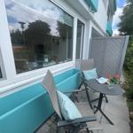 Terrasse mit zwei Stühlen, Tisch und Blumen. Große Fensterfront und grüne Hecke.