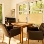 Dining area with wooden table and four brown chairs. Large windows and glass door to garden.