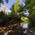 Fluss durch Wald mit Ruinen im Hintergrund