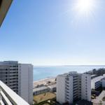 Blick vom Balkon auf das Meer und umliegende Gebäude unter strahlendem Sonnenschein.