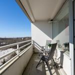 Balcony with two chairs and a small table. View over rooftops and trees under clear sky.
