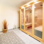 Holzsauna mit Sitzbänken und Glasfront. Nebenraum mit Stuhl, Tisch und Pflanze.