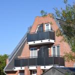Zwei Balkone mit schwarzen Geländern an einem roten Ziegelhaus unter blauem Himmel.