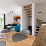 Essbereich mit Holztisch und Stühlen. Treppenhaus und Wohnbereich mit Sofa und Wandbild.