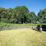 Grüner Garten mit Holzzaun und Terrasse neben einem Gebäude mit Strohdach.