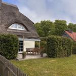 Haus mit Strohdach, Terrasse mit Tisch und Stühlen, umgeben von grünen Hecken.