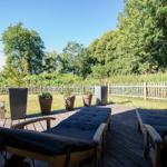 Holzterrasse mit Liegestühlen, Pflanzen und Gartenzaun im Hintergrund.