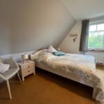 Schlafzimmer mit Dachschräge, Bett, Stuhl und Fenster mit Blick auf Grün.