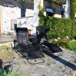 Two black lounge chairs on stone pavers in front of a house with green hedge.