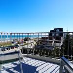 Terrasse mit Sitzgelegenheiten und Meerblick. Hintergrund: Strand und Gebäude.