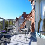 Balkon mit Stuhl, Tisch und Blumen. Blick auf Dach und Grün.