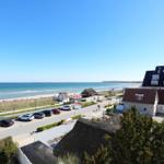 Meerblick mit Strand, Parkplatz und Häusern in der Ferne.