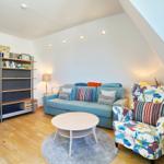 Wohnzimmer mit Sofa, Sessel und Regal unter schrägen Dachdecken.