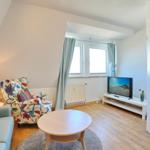 Wohnzimmer mit Sitzgelegenheiten, Fernseher und Fenster mit Vorhängen.
