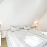 Schlafzimmer mit Doppelbett, zwei Nachttischen und Lampen. Weiße Wände und schräge Decke.