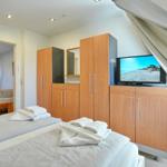 Zimmer mit zwei Betten, Schrank und Fernseher. Blick in angrenzendes Zimmer.