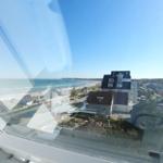 Blick vom Fenster auf Strand und Meer mit Häusern im Hintergrund.
