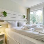 Schlafzimmer mit weißem Bett, Nachttisch und Fenster zum Balkon.