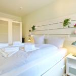 Ein Schlafzimmer mit weißem Bett, Nachttisch und Kleiderschrank. Auf dem Bett liegen Handtücher.