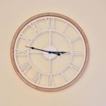 A wall clock with a wooden frame and Roman numerals on the wall.
