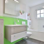 Bathroom with green accent, sink, shower, and window.