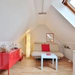 Attic room with sofa bed, table and red sideboard under sloped ceiling.