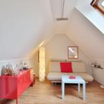 Attic room with sofa, table, and red sideboard under sloped ceiling.