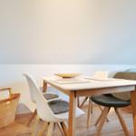Dining area with table and chairs, sofa in background, basket on wall.